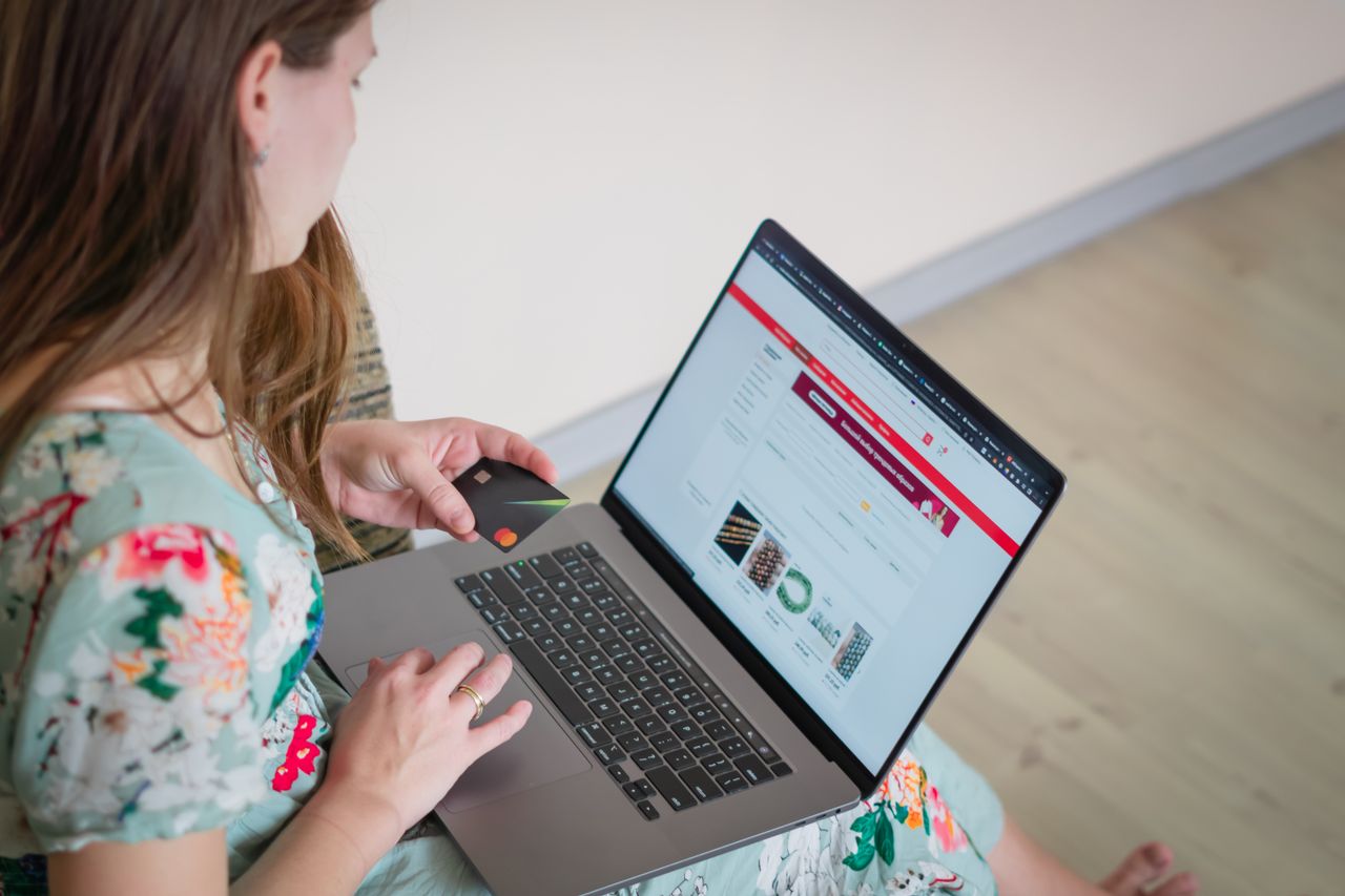 team-02 Woman in floral dress shopping online with a laptop and credit card indoors.